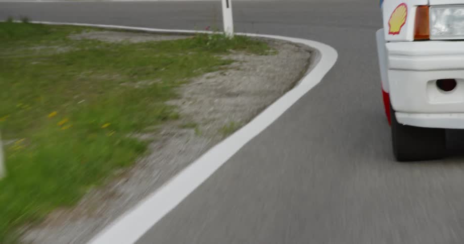 A car with a shell logo travels on a curvy road