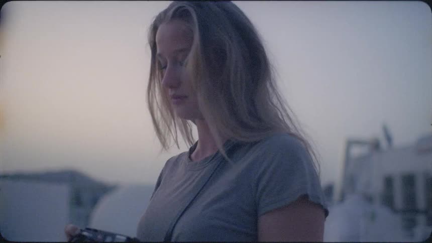 A woman is lifting her camera to take photos from a rooftop at dusk
