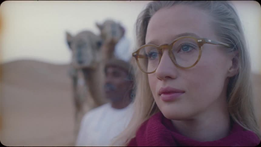 Woman looking off in the desert with a man leading a camel behind her