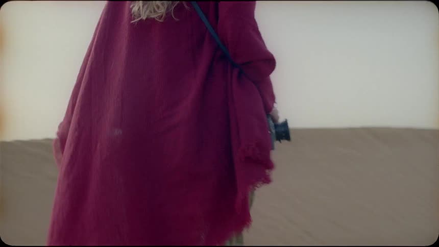 A woman walks through the sand carrying a camera
