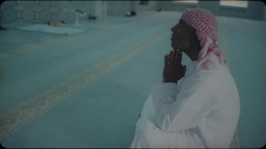 An arab man is sitting on the ground inside a mosque praying in daylight
