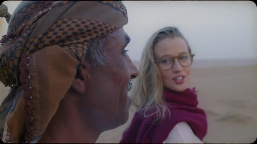 Woman talks to a man while walking in the desert leading a camel