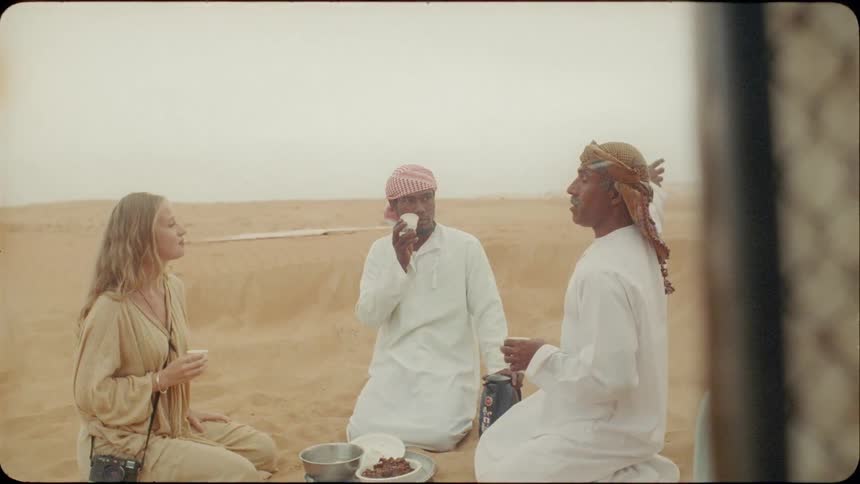 Woman sits and drinks tea with two men in the desert
