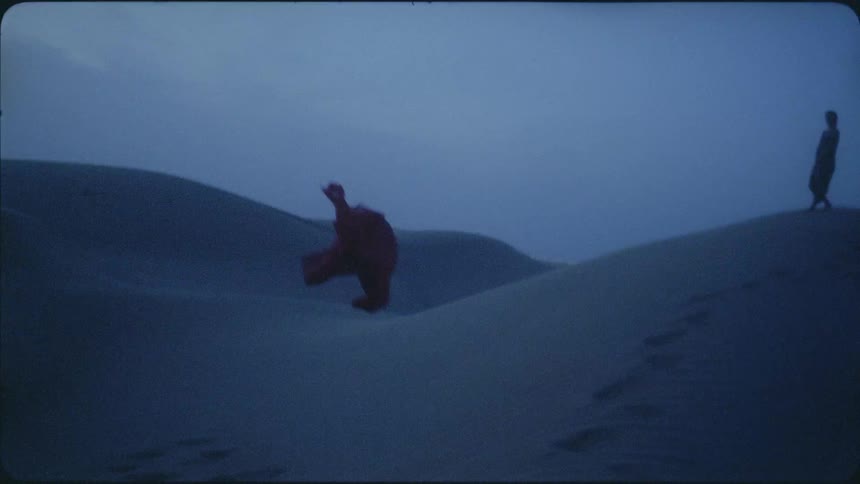 Red cloth floats through the air and lands on a sandy hill in the evening