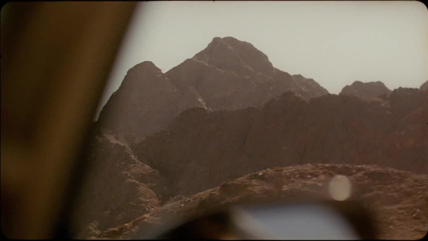 A car travels past rocky ridges and peaks on a sunny day