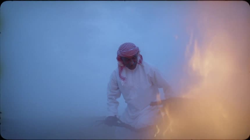Man in a white gown tosses sticks onto a bonfire