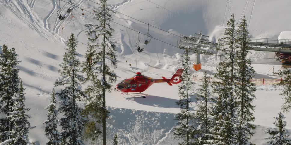 A red helicopter sits on the top of a snow covered mountain