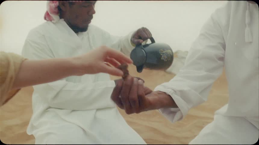 Woman and men kneel on the sand as they eat