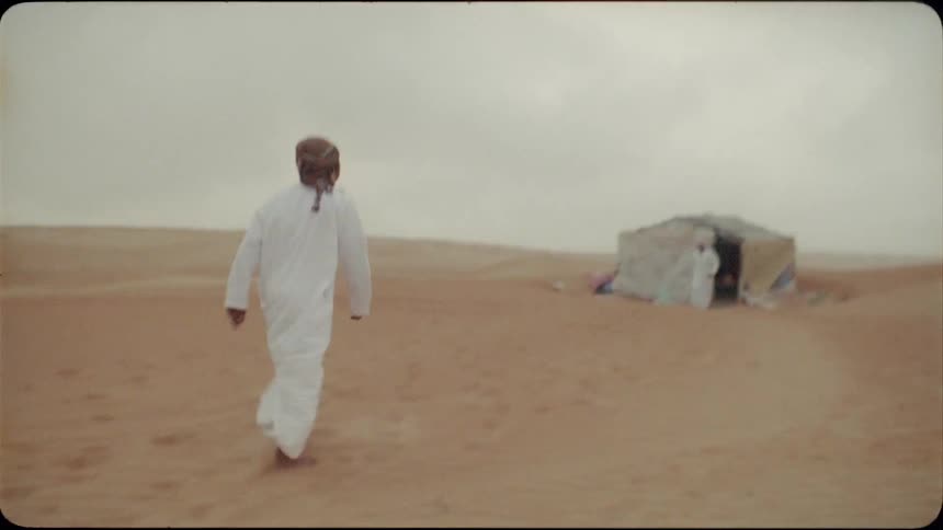 An arab man walks toward another near a tent in the desert