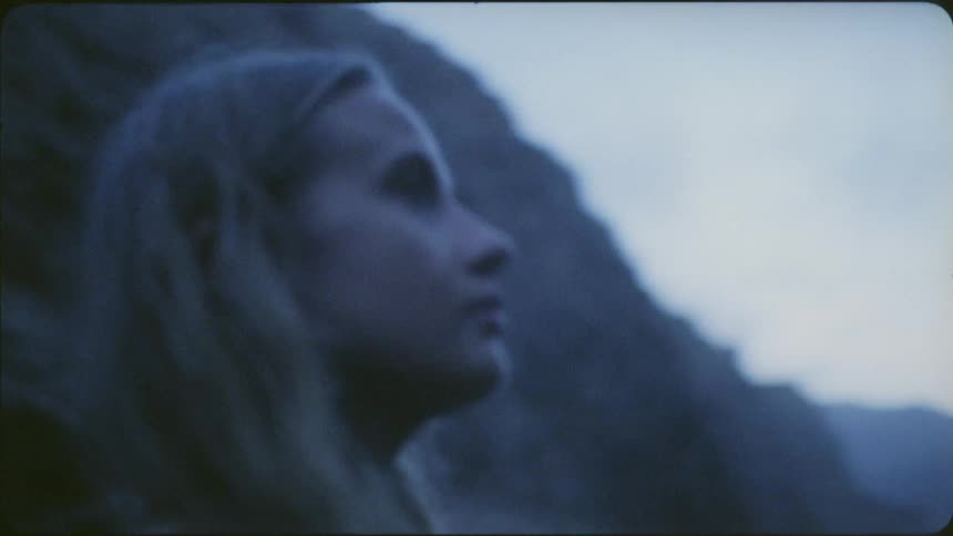 A woman wearing a backpack pauses and looks up at hills