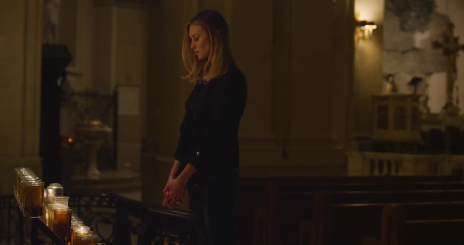 Woman standing and praying in a church next to candles