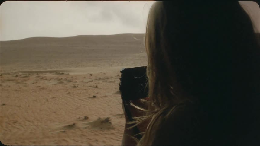 A woman photographs from a moving vehicle in the desert