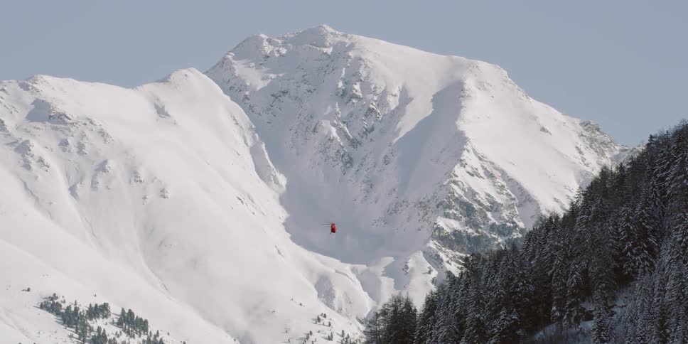 A helicopter flies between the snow covered mountains