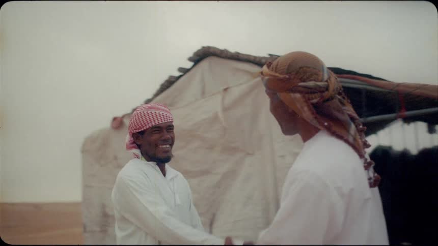 Two men emerge from a tent in the desert and shakes hands