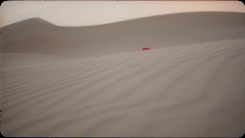 Red cloth floats through the air and lands on a sandy hill in the evening
