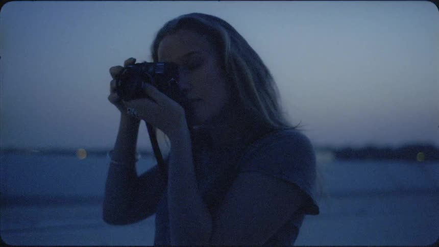 A woman walks on the beach at dawn taking photographs