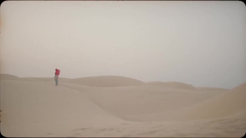 The wind blows a red scarf against a woman standing on the dunes