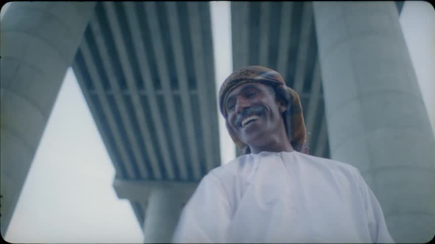 Man standing under a bridge smiles and waves his arm