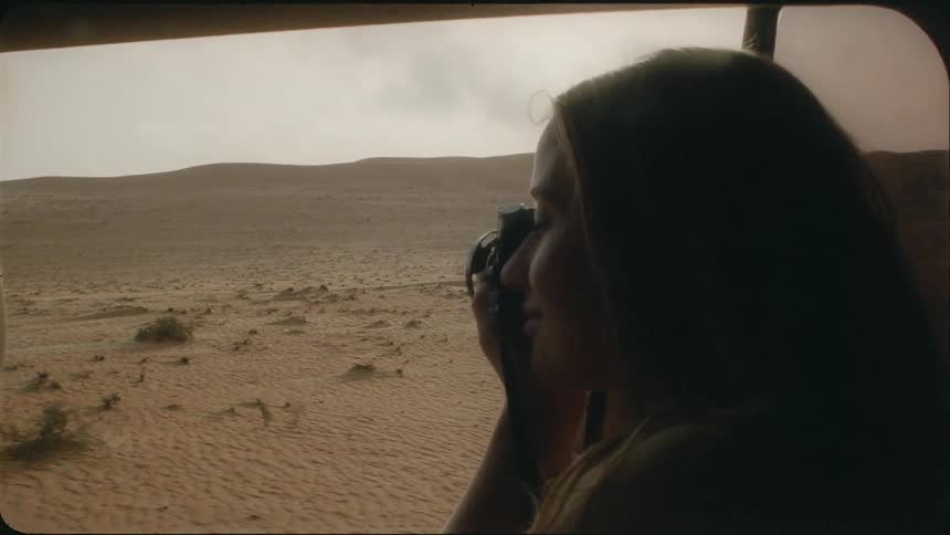 The woman is taking photographs of the desert from the vehicle