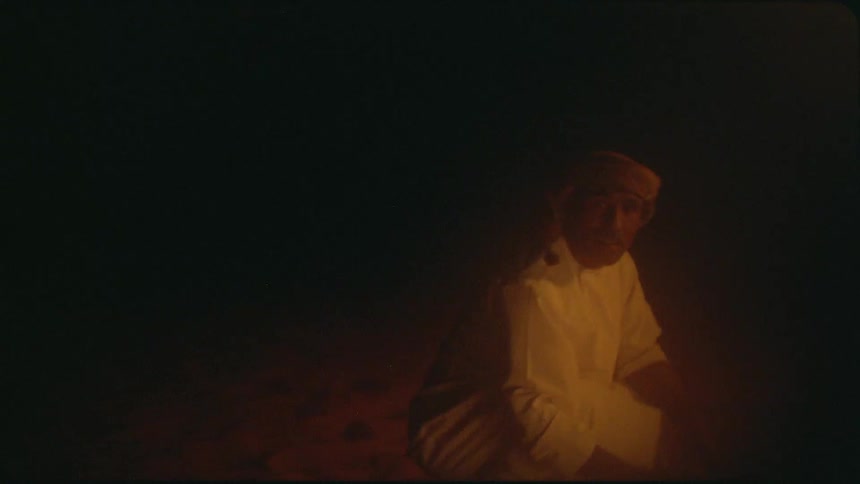 A man feeds a campfire in the desert then stands
