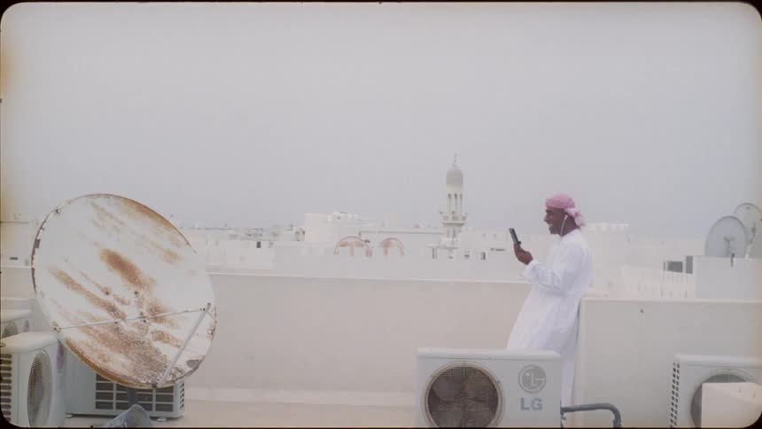 An arab man is standing on a rooftop talking on his cellphone in daylight