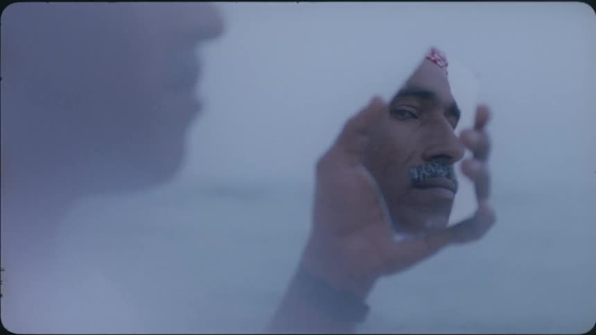 A man holding a mirror fragment showing his reflection