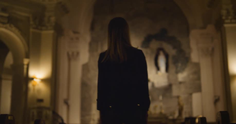 A young, blonde woman standing and turning around as she looks at a church ceiling