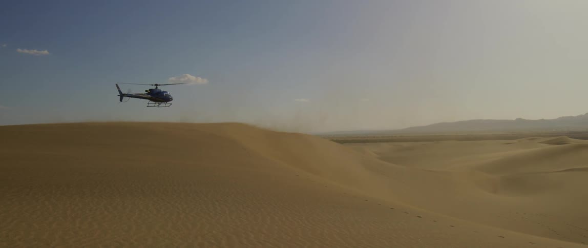 Helicopter hovers over a vast sandy landscape
