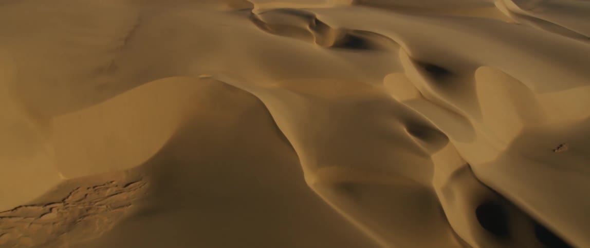 The sand dunes run across the desert below
