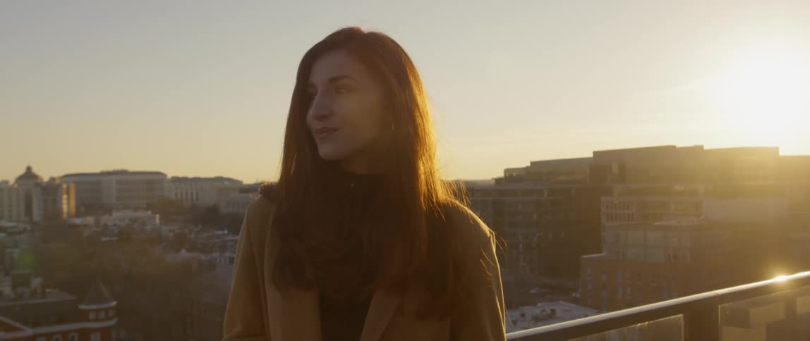 Woman stands on a rooftop at sunset in the city