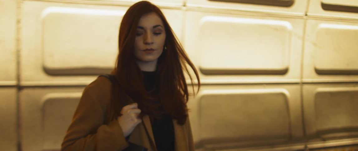 A woman stands with her back to a subway train pulling out of the station