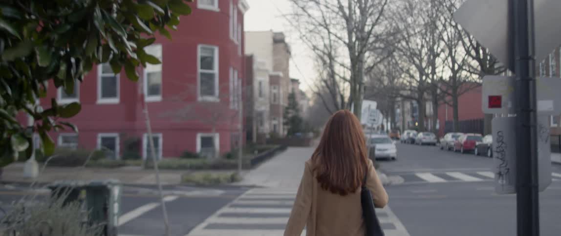 Woman with a handbag over her shoulder walks down a city sidewalk