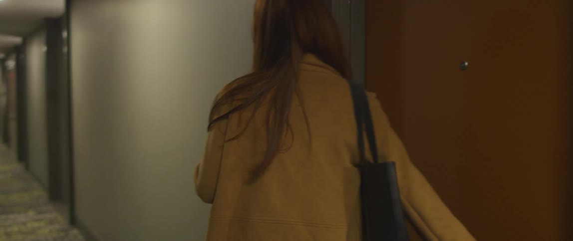 Woman opens a brown door and walks down a hallway