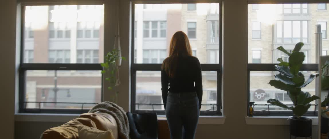 A woman stands up from a couch to look out the window