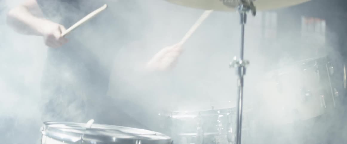 A man plays the drums as fog billows around him