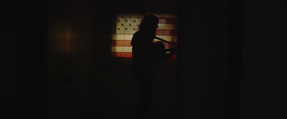 Person standing in the shadows holding a guitar