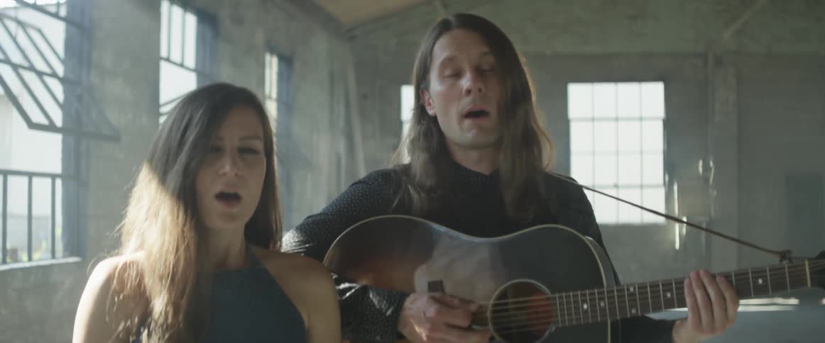 A man and woman sing and play guitar
