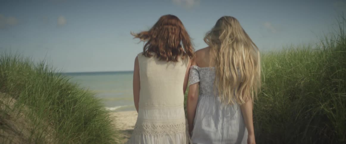 Two women walk towards the beach under a blue sky