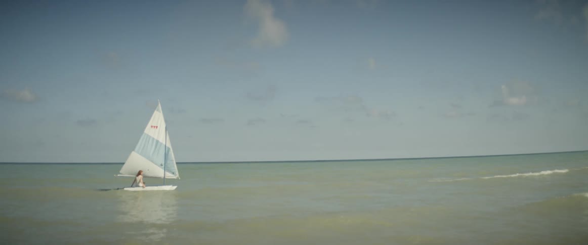 Two girls are sailing a boat in the shallows of a beach on a sunny day