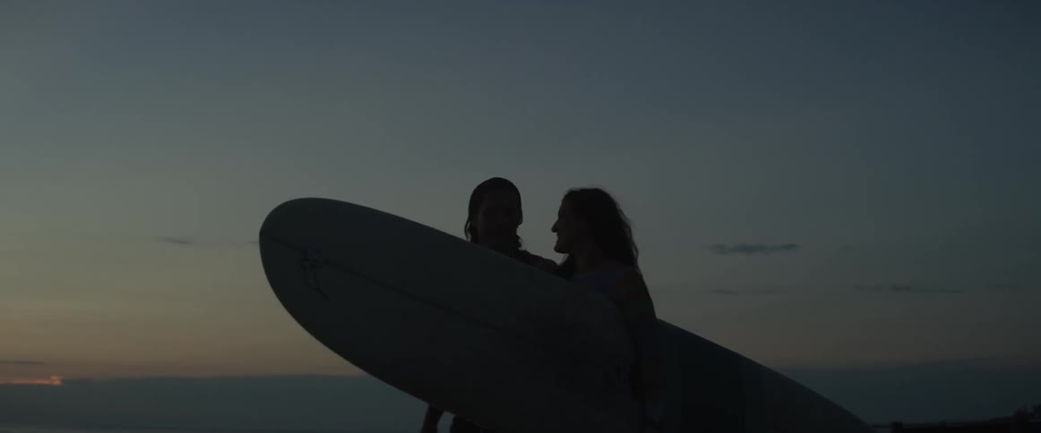 Woman carries a surfboard as she walks with a man on the beach
