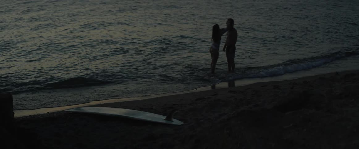 Woman touches a man's hair on the beach at sunset