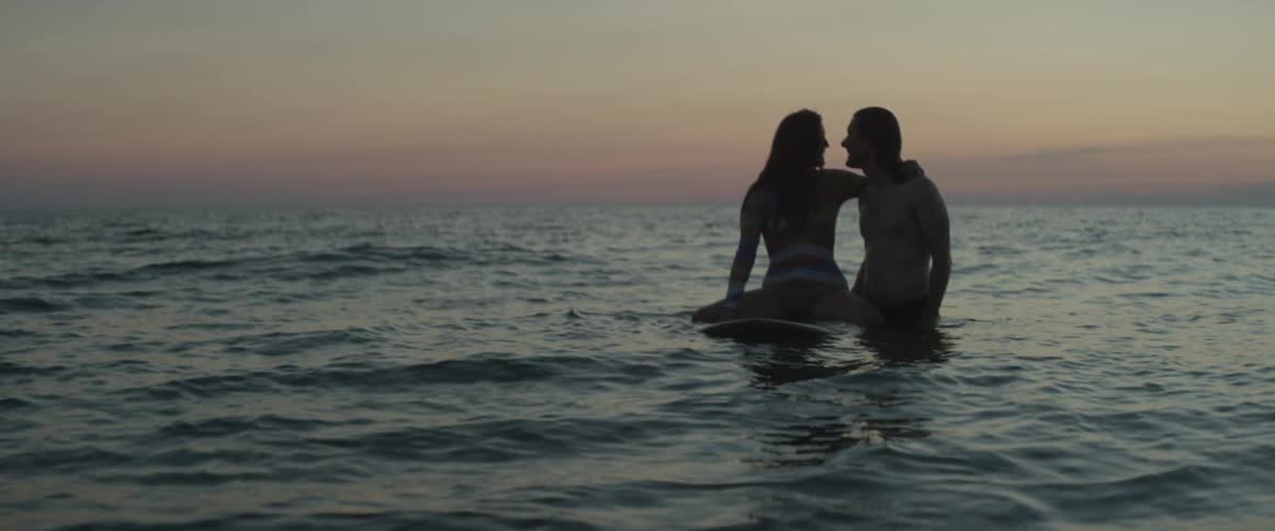 A woman sitting on a surfboard holds onto a man in the ocean
