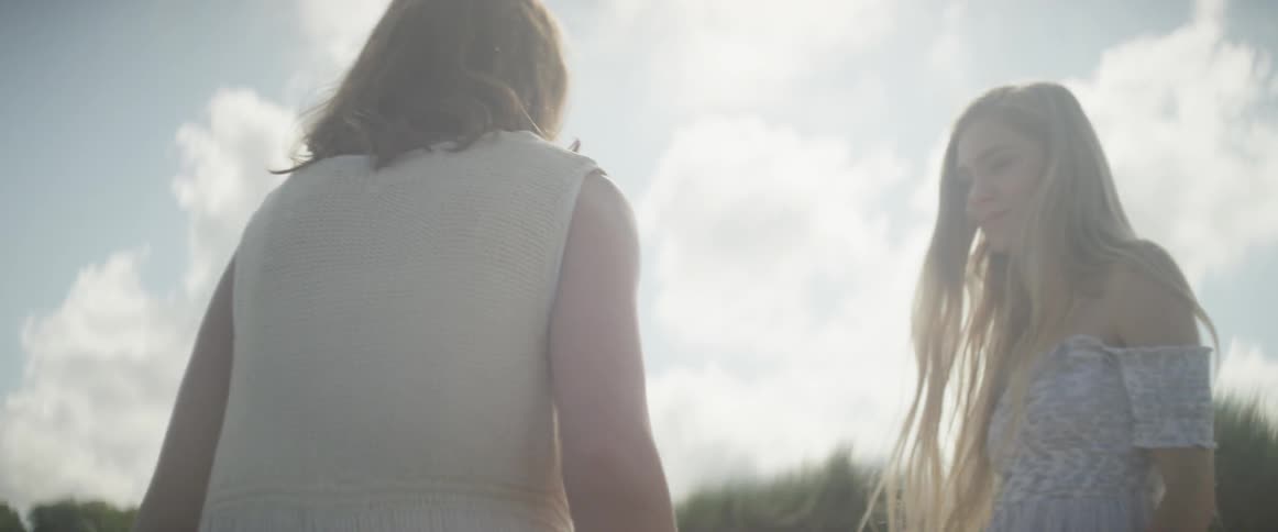 Two women walk under the cloudy blue sky