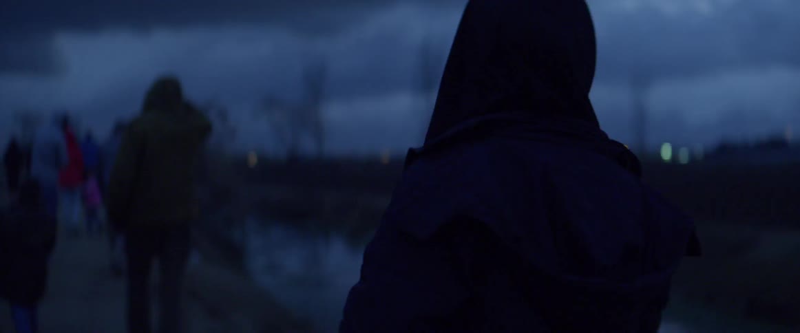 Hooded figure walks outside at night