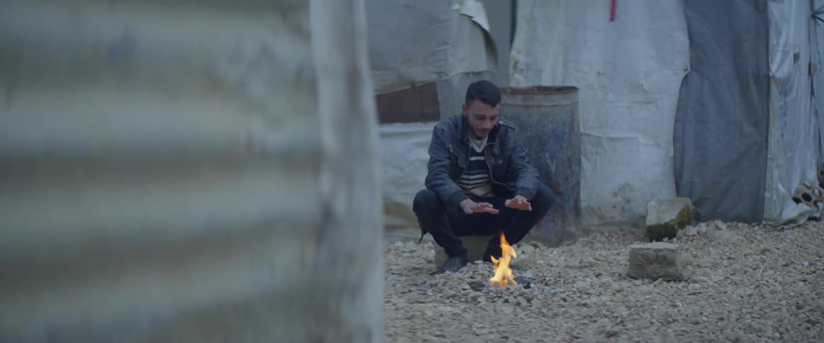 A man sits by a small campfire