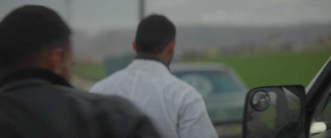 Two men walk on the field and open the car trunk