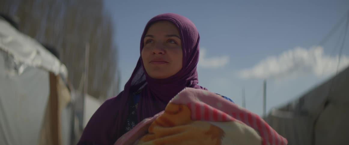 A woman carrying a baby in a blanket smiles as she walks on a sunny day