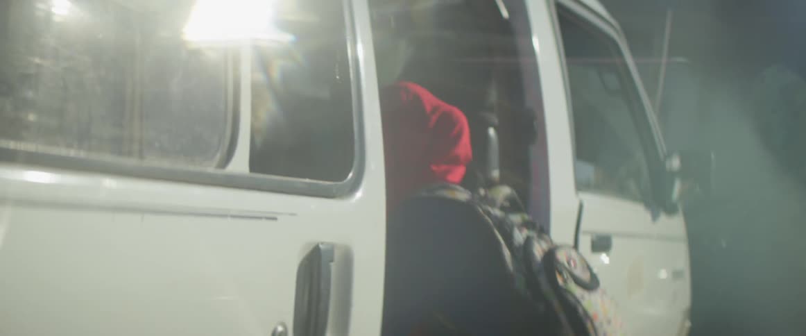 A girl wearing a headscarf and a backpack gets into a van