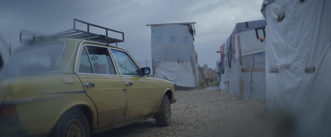 A car is parked near a tent city on a cloudy day