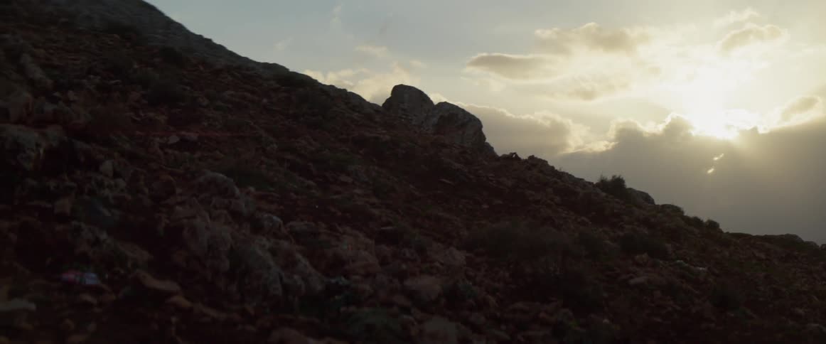 The sun is setting behind the clouds by the hill
